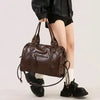 A brown vintage washed leather tote bag carried by a person wearing a black jacket.