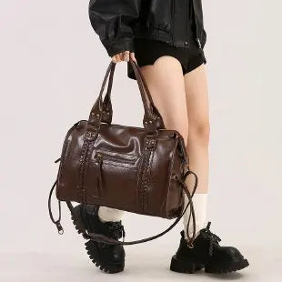 A brown vintage washed leather tote bag carried by a person wearing a black jacket.