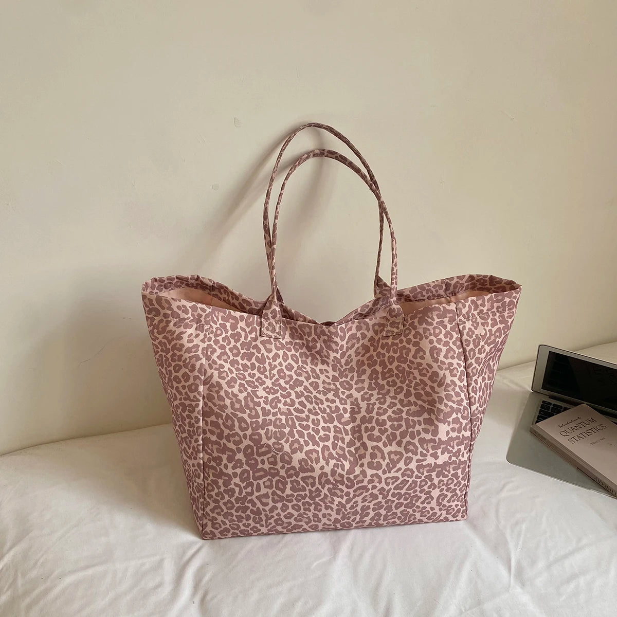 A beige leopard print canvas tote bag with long handles resting on a white surface.