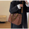 A person is holding a brown textured corduroy tote bag with adjustable straps against a black coat.