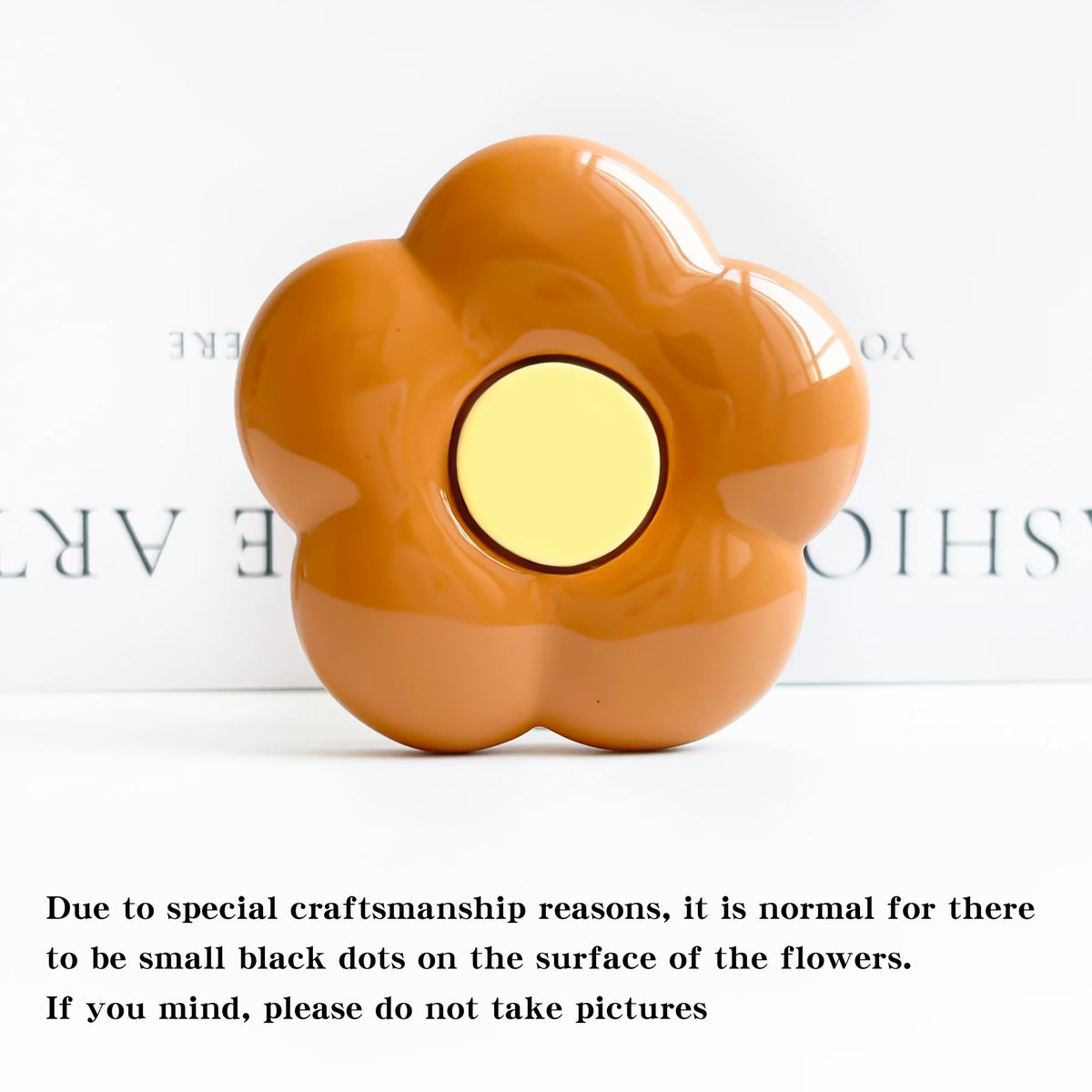 A smooth, orange-colored flower-shaped phone grip ring stand with small black dots on the surface.