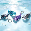 Three blue and purple ocean star-themed devil ray figurines with silver clasps resting on a light blue surface.
