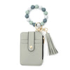 A light gray leather card holder with a beaded tassel keychain attached.