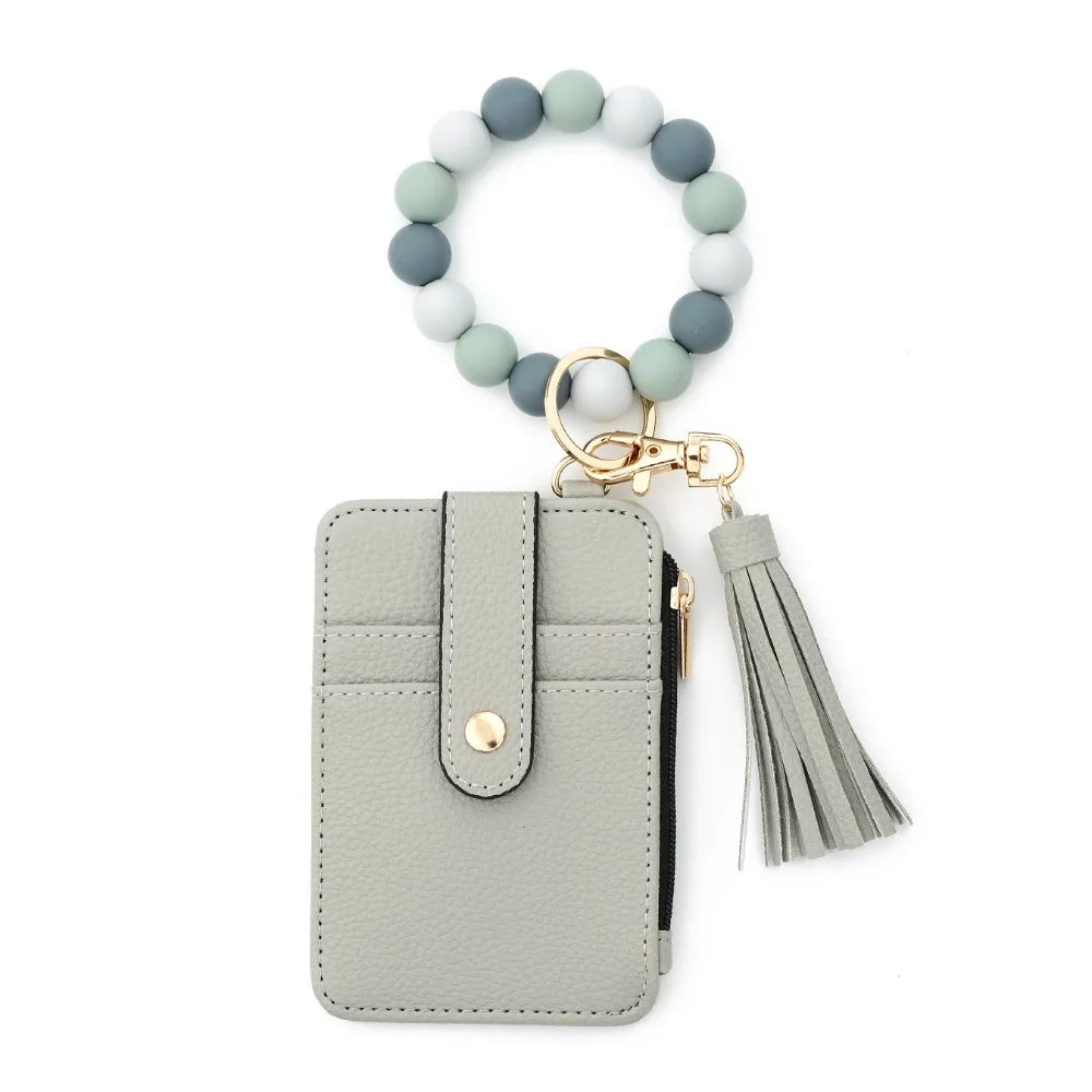 A light gray leather card holder with a beaded tassel keychain attached.