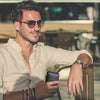 A man wearing sunglasses sits at a table holding a black minimalist wallet.
