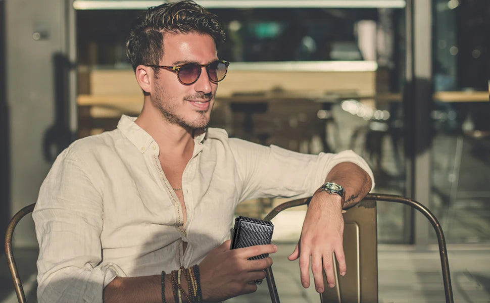 A man wearing sunglasses sits at a table holding a black minimalist wallet.
