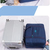 A dark blue foldable travel duffel bag is shown with various items like rolled clothes and a silver suitcase.