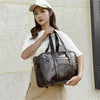 A woman wearing a white t-shirt and apron holds a brown leather shoulder bag in a casual outdoor setting.