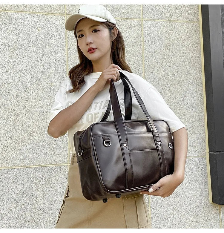A woman wearing a white t-shirt and apron holds a brown leather shoulder bag in a casual outdoor setting.