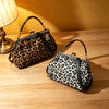 A black and brown leopard print faux leather handbag with a top handle and crossbody strap resting on a wooden surface.