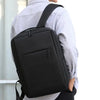 A person is wearing a black versatile USB-rechargeable laptop backpack over a light gray shirt.