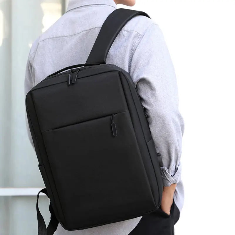 A person is wearing a black versatile USB-rechargeable laptop backpack over a light gray shirt.