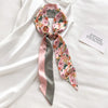 Écharpe florale de soie rose et vert nouée en nœud, posée sur un tissu blanc avec une petite carte.