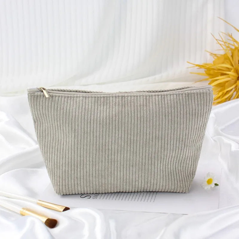 A light gray corduroy makeup organizer bag with an octagonal design resting on white fabric.