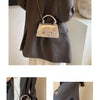 A close-up of a silver gold square crossbody bag with a chain strap worn by a woman in a gray blazer.