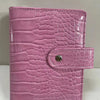 A pink crocodile leather ring binder notebook with a stitched closure.