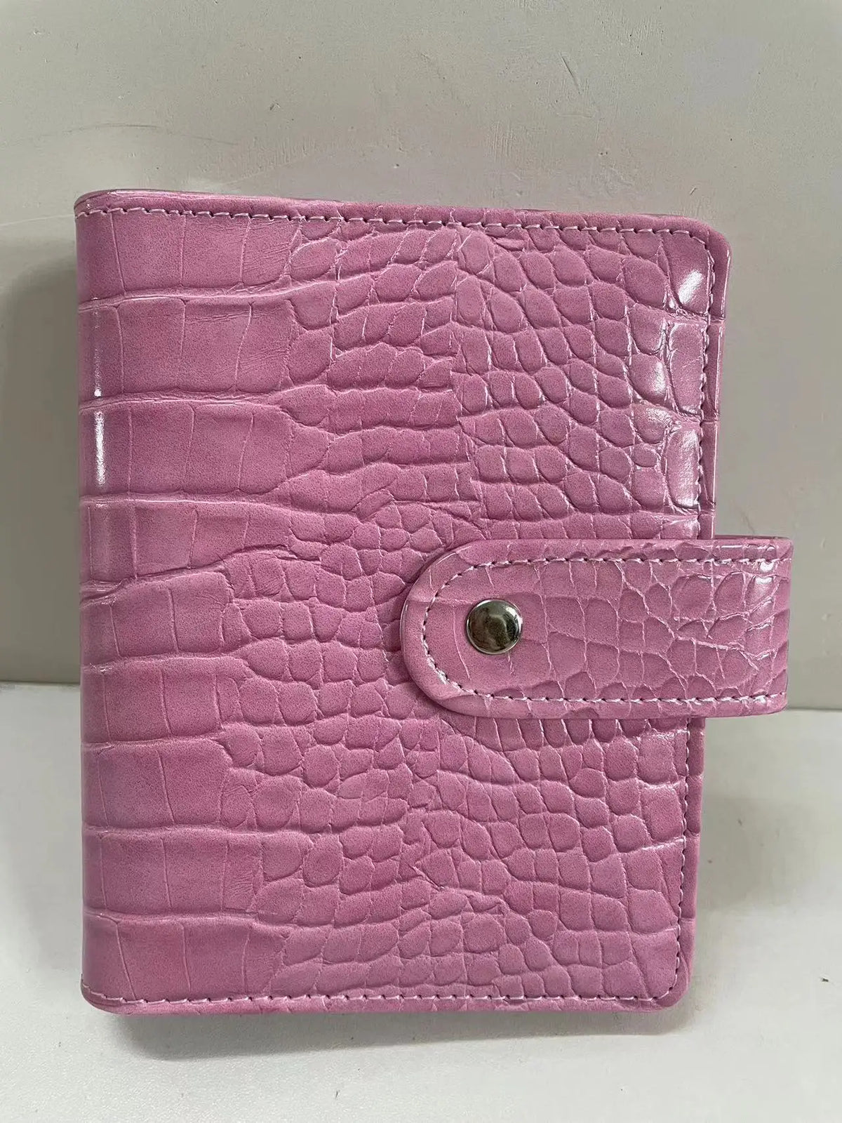 A pink crocodile leather ring binder notebook with a stitched closure.