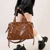 A brown vintage washed leather tote bag carried by a person wearing a black jacket and skirt.