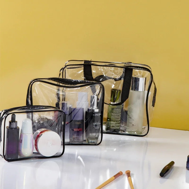A set of three clear PVC travel toiletry bags with black straps resting on a white surface.
