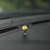 Eine kleine Glasvase mit einer Ansammlung gelber Rosen auf einer dunklen Auto-Innenausstattung.
