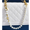 A pearl and gold letter charm necklace displayed against a white quilted bag.