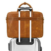 A brown vintage genuine leather briefcase with black and silver handles resting on a silver rolling suitcase.
