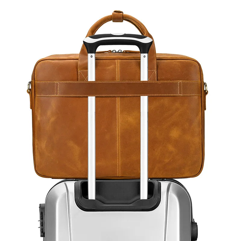 A brown vintage genuine leather briefcase with black and silver handles resting on a silver rolling suitcase.