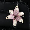 A realistic orchid flower keychain with pink and white petals hangs from a silver chain against a black leather handbag.