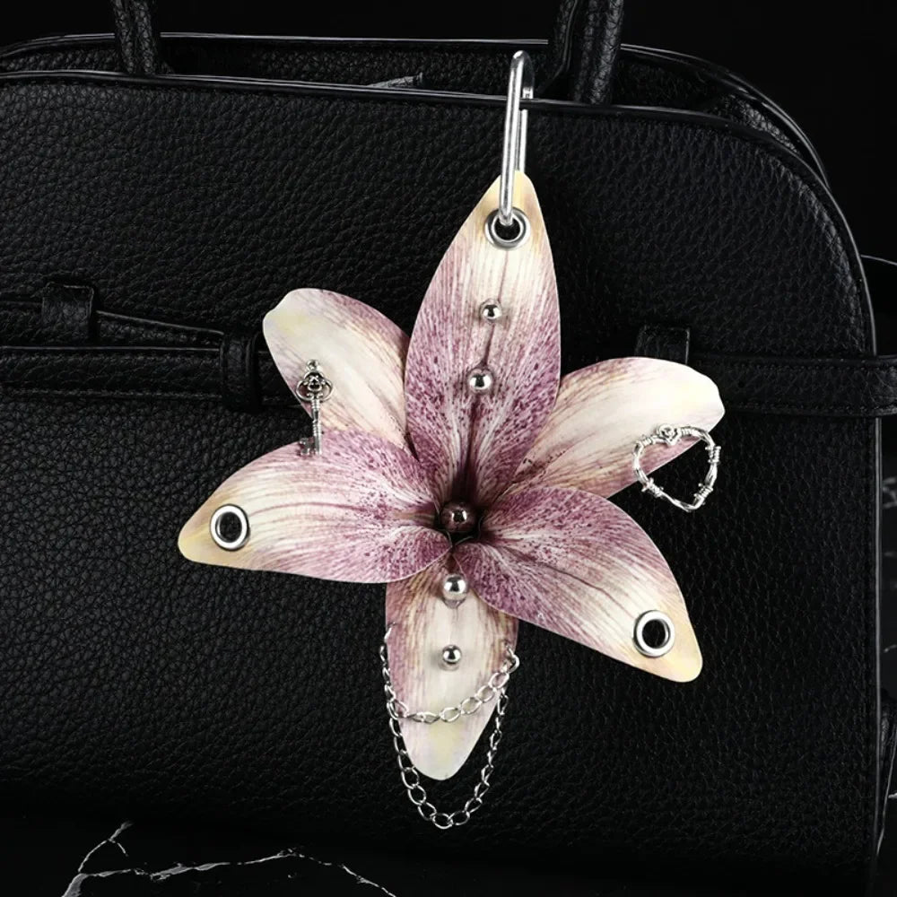 A realistic orchid flower keychain with pink and white petals hangs from a silver chain against a black leather handbag.