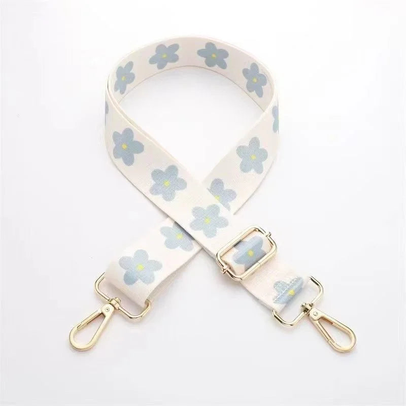 A beige nylon bag strap with a floral pattern and gold-toned hardware.