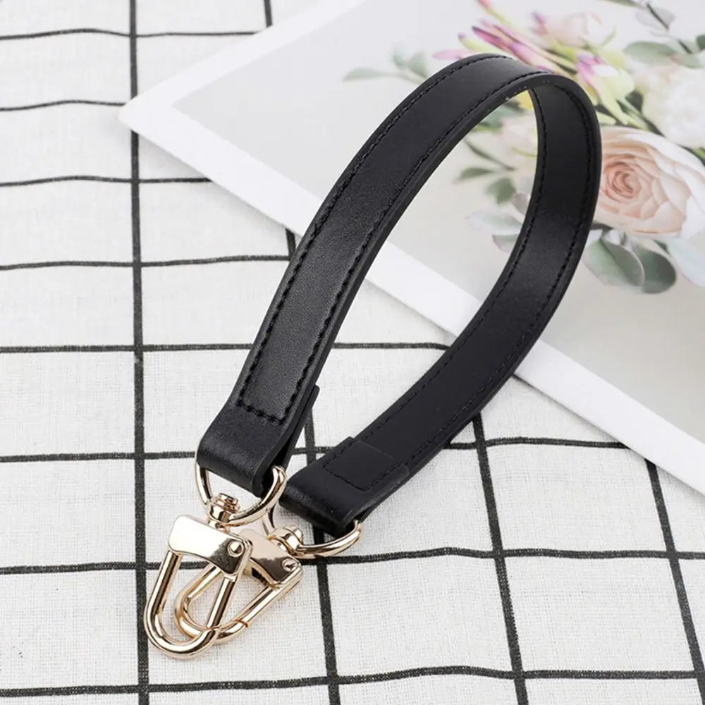 Black genuine leather replacement shoulder strap with gold hardware lying on a white checkered surface.