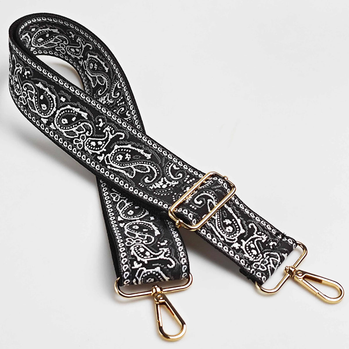 Correa de cuero con patrón blanco y negro y herrajes dorados para un bolso cruz ajustable.