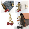 A crystal fruit charm keychain featuring red cherries attached to a gold-colored bag accessory.