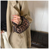 A hand wearing a gold ring holds a leopard print PU leather mini tote handbag against a beige trench coat.