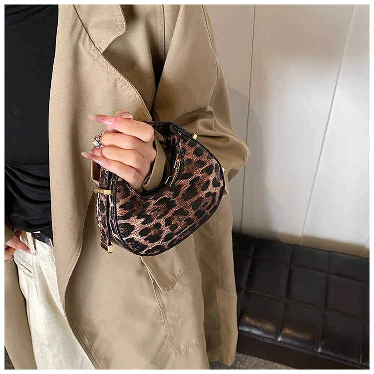 A hand wearing a gold ring holds a leopard print PU leather mini tote handbag against a beige trench coat.