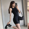 A woman wearing a black sleeveless bodycon tank dress and black boots posing indoors.