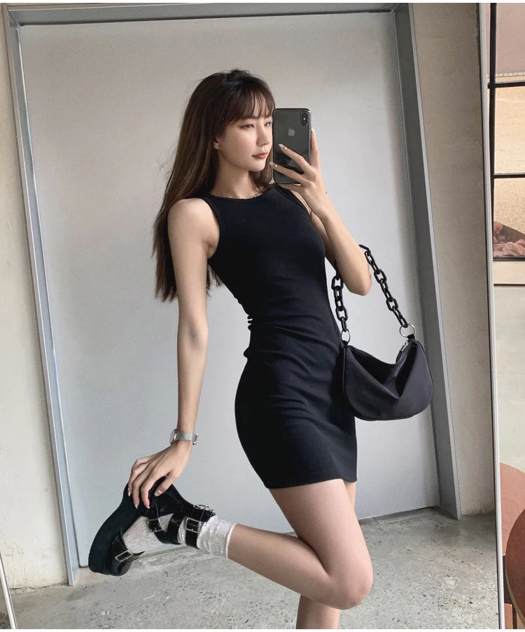 A woman wearing a black sleeveless bodycon tank dress and black boots posing indoors.