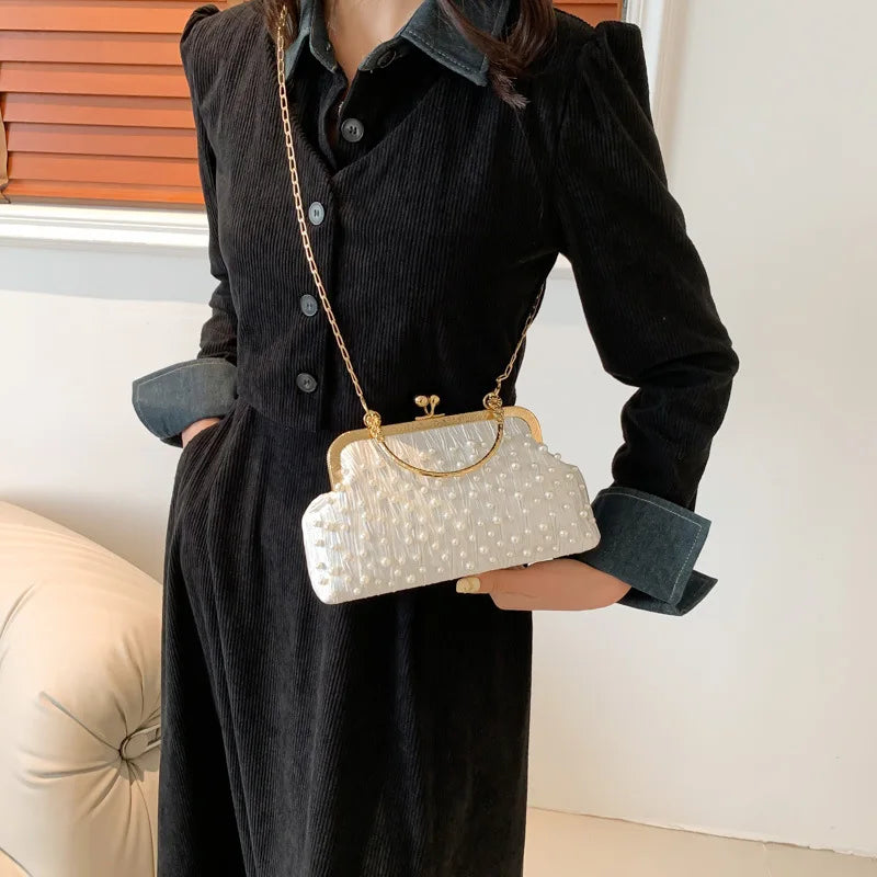 A woman models a pearl embellished crossbody shoulder bag against a white background.
