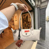 A hand holds a white leather shoulder bag with gold hardware in a store setting.