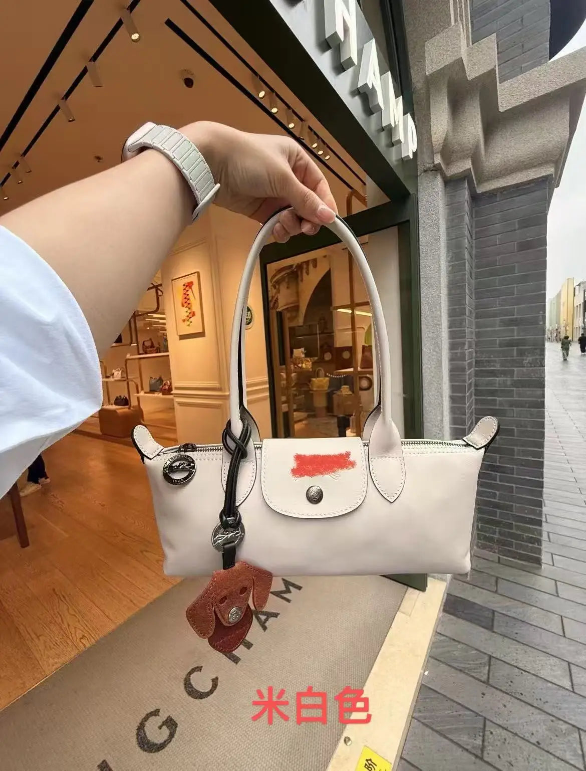 A hand holds a white leather shoulder bag with gold hardware in a store setting.