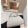 A light silver pleated glitter evening handbag with a top handle and chain strap is displayed on a black fabric.
