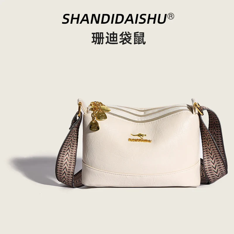 A cream-colored luxury PU leather crossbody handbag with gold hardware and a patterned strap.