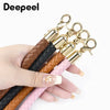 A hand holds a pair of gold-toned leather bag handles with metal buckles.