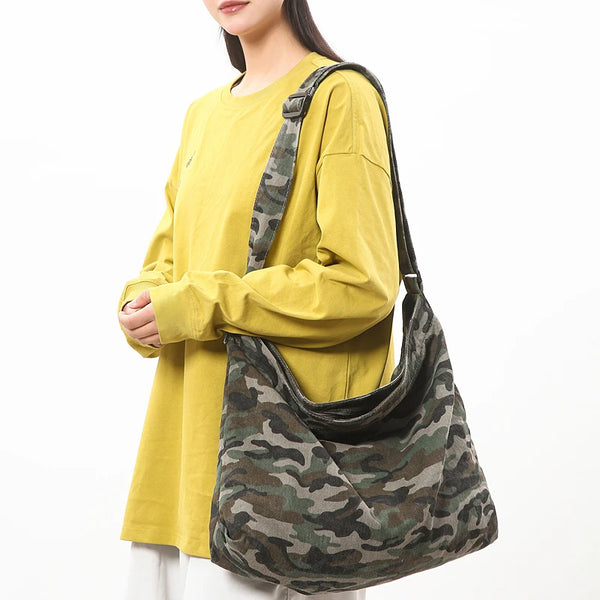 A woman is holding a canvas camouflage shoulder bag with an adjustable strap and wearing a yellow shirt.