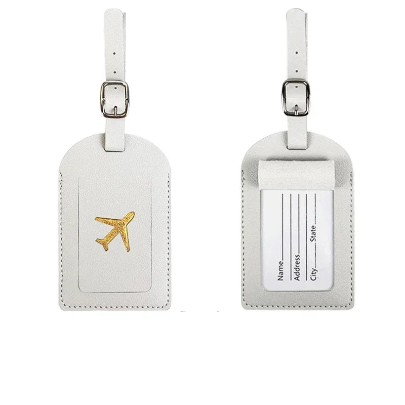 A pair of light beige PU leather luggage tags with silver hardware and a gold airplane design.