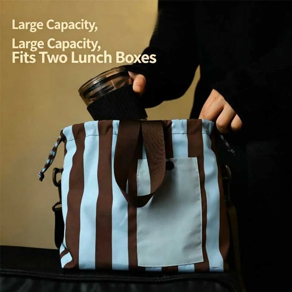 A person is holding a striped insulated lunch bag with a brown strap and a glass container.