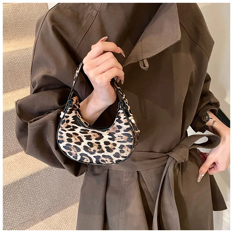 A person holds a leopard print PU leather mini tote handbag against a brown trench coat.