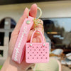 A pink silicone heart beach bag keychain is held in a hand against a blurred outdoor background.