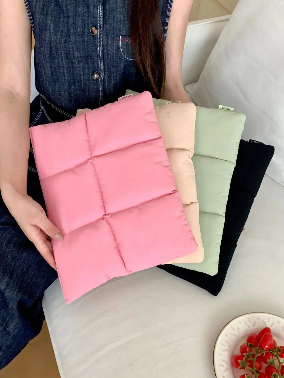A stack of pink, beige, and green quilted laptop sleeves resting on a white surface.