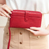 A woman holds a red PU leather zipper clutch wallet against a beige skirt.